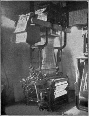 Fig. 73.   The Jacquard loom. Notice the cards with punched holes above it. They affect the pattern. Can you find the cloth which is being woven ?