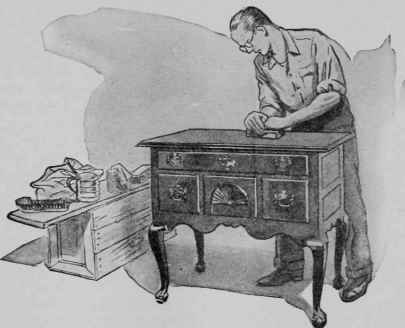 The final polish is given to the oiled and waxed top of a low boy with a rubbing block.
