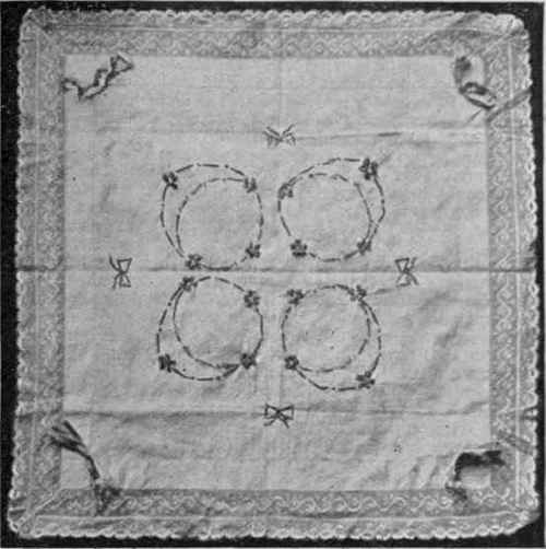 A cushion cover edged with Valenciennes lace, and worked in a garland design in net shadow embroidery upon a gentleman's fine cambric handkerchief